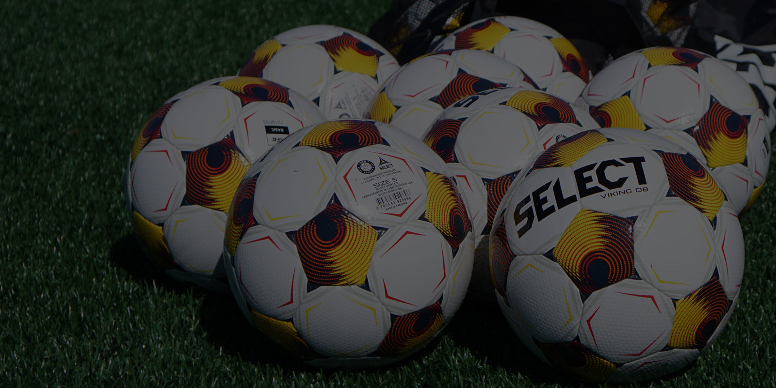 White soccer balls with navy, yellow, and orange accents on a soccer field with a faded black overlay