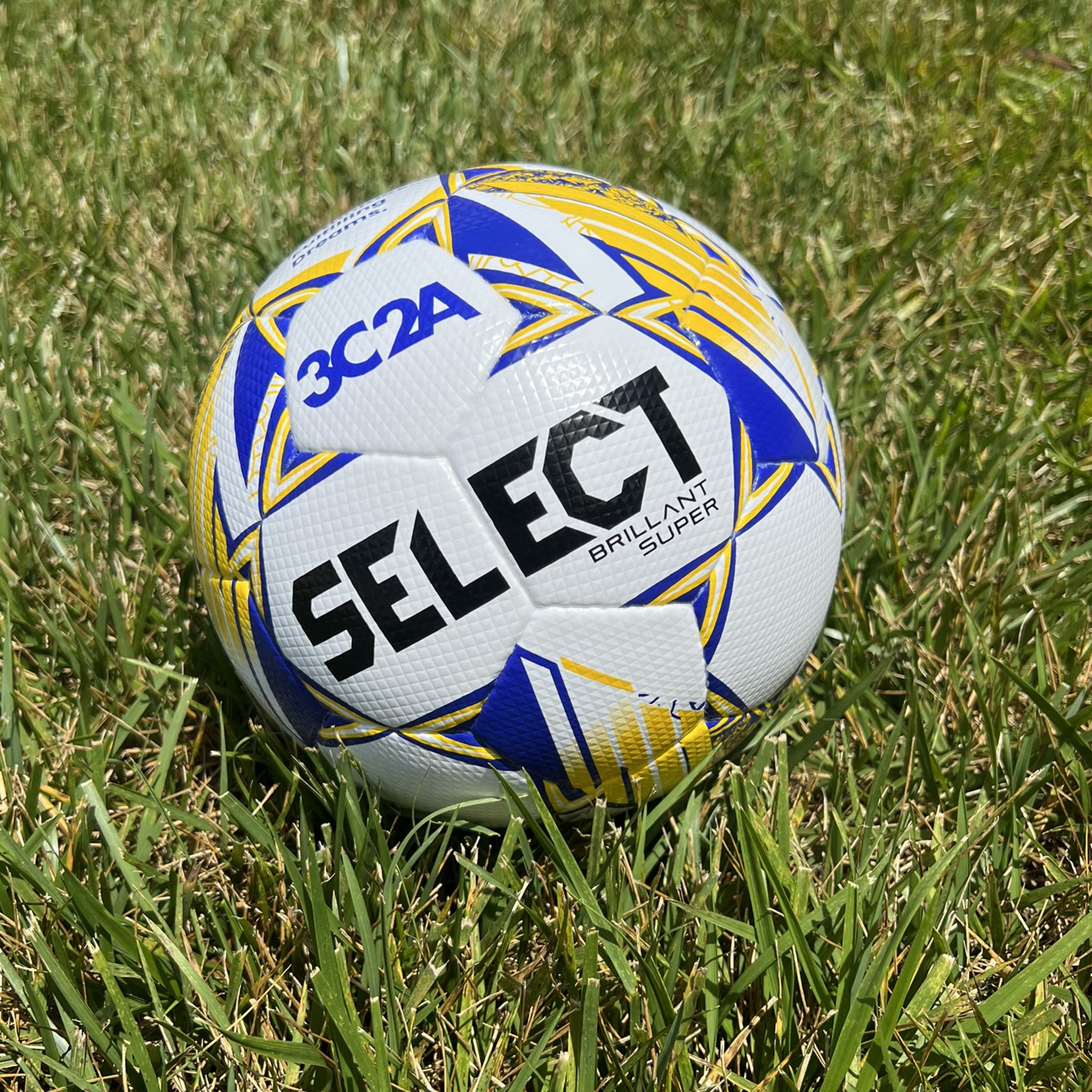 White soccer ball with blue and yellow accents and 'Select' branding on a grass field