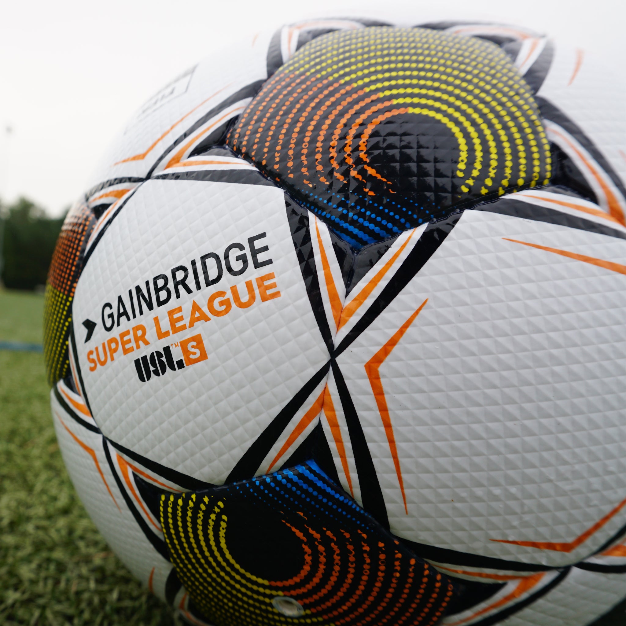 White soccer ball with black pentagons, orange and yellow accents and 'Select' branding on a white background. Official match ball of the Gainbridge Super League 2025/26 season #color_white/orange