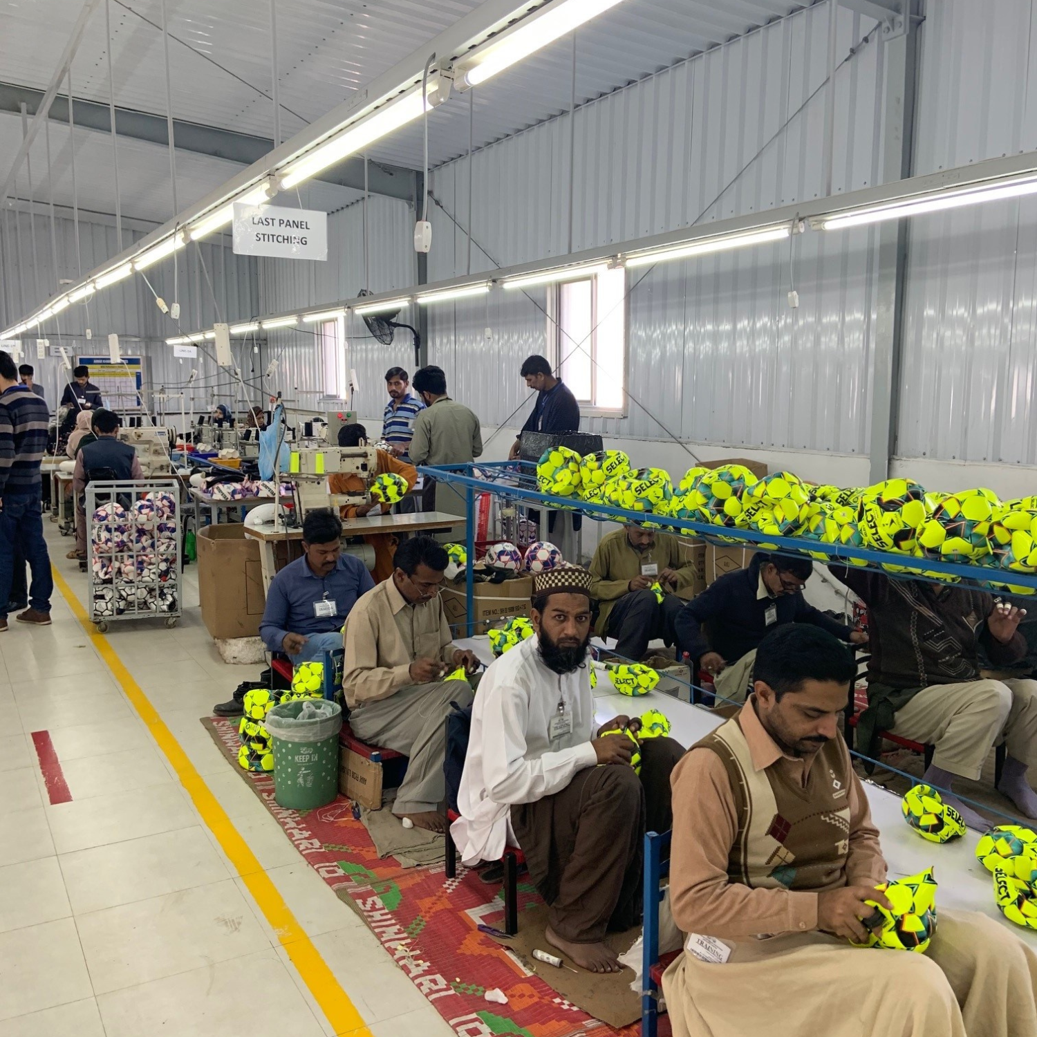Factory workers stitching yellow soccer balls