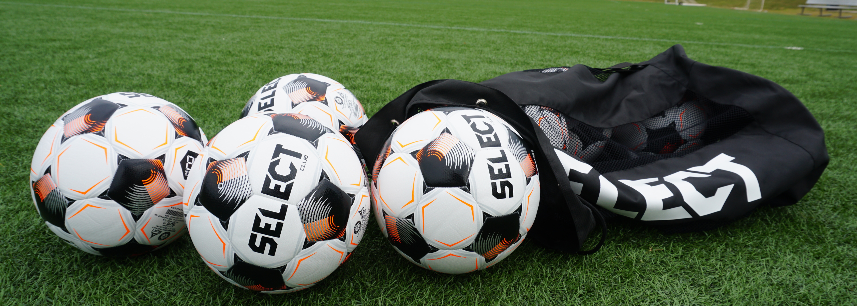 SELECT brand soccer balls with a black drawstring bag resting on green artificial turf.