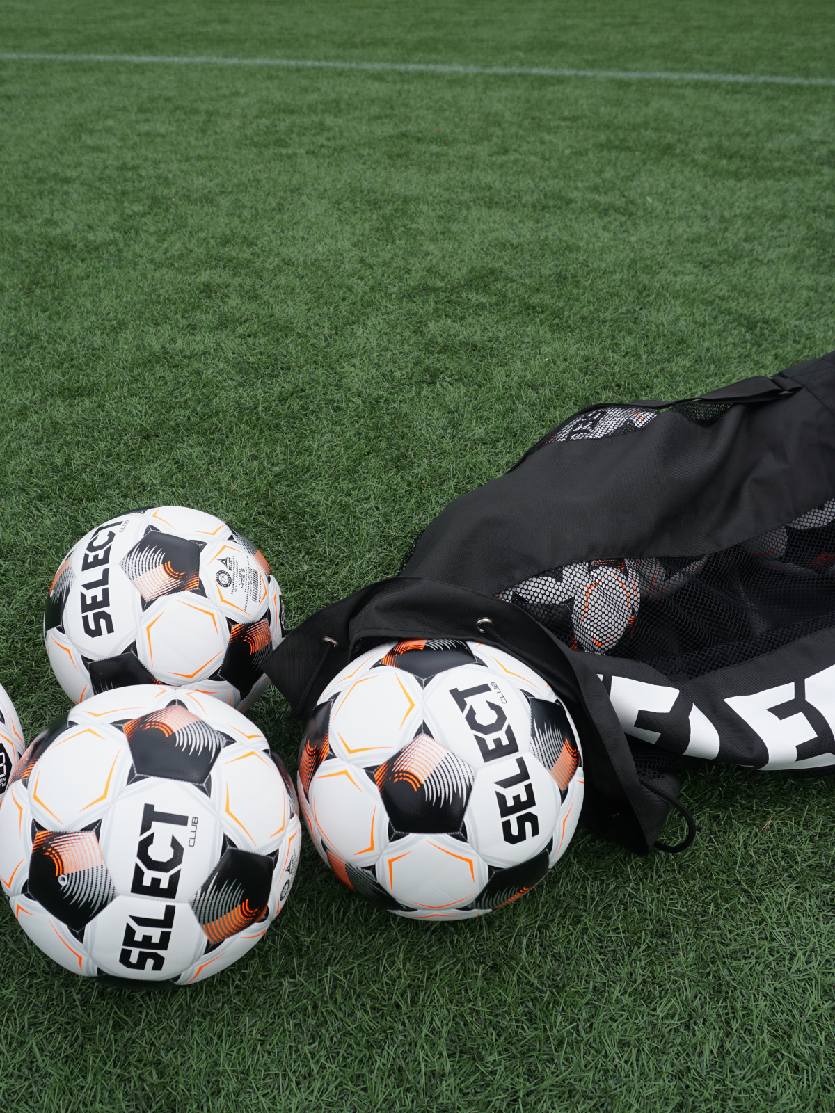 SELECT brand soccer balls with a black drawstring bag resting on green artificial turf.