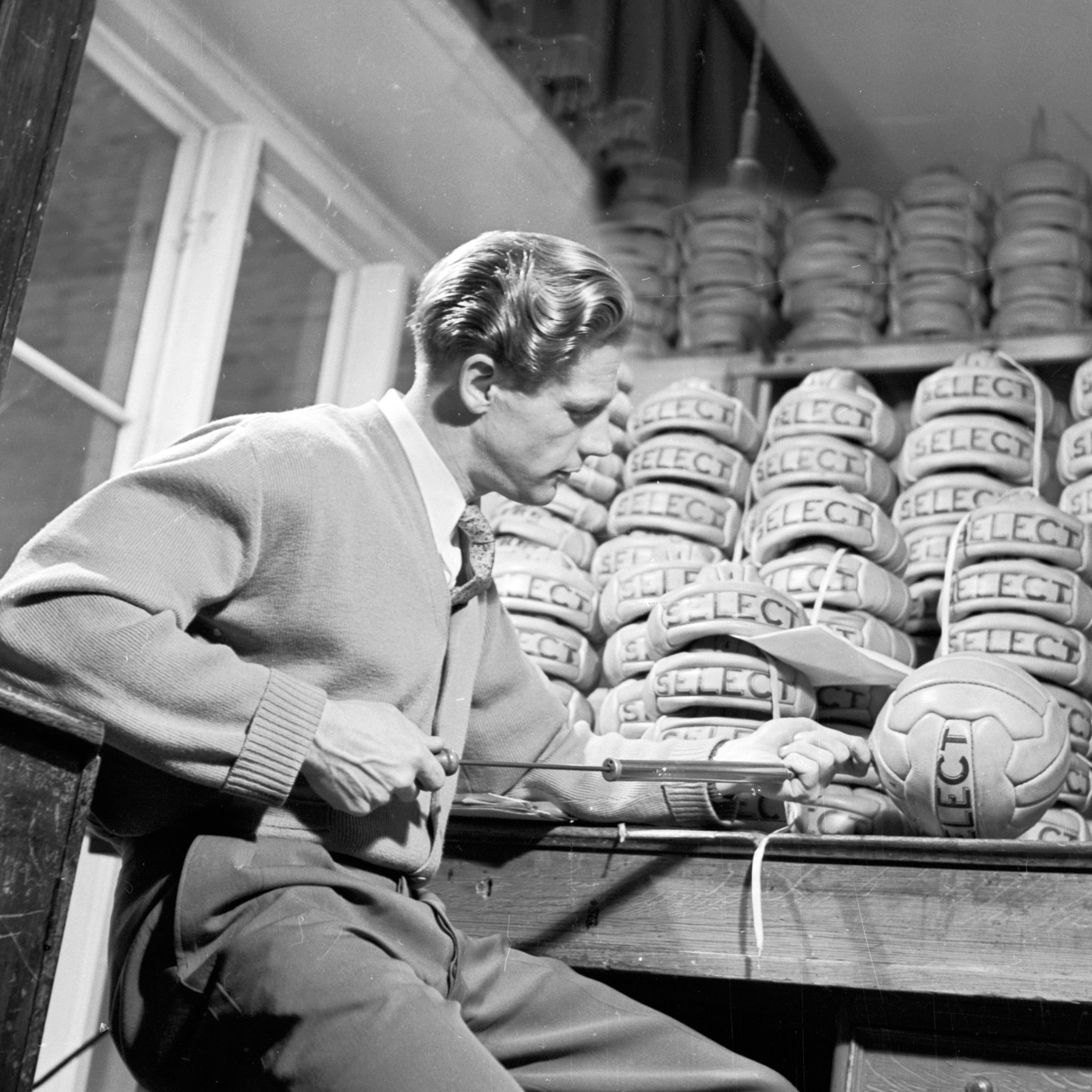 Select founder Eigil Nielsen inflating a soccer ball with a stack of soccer balls in the background