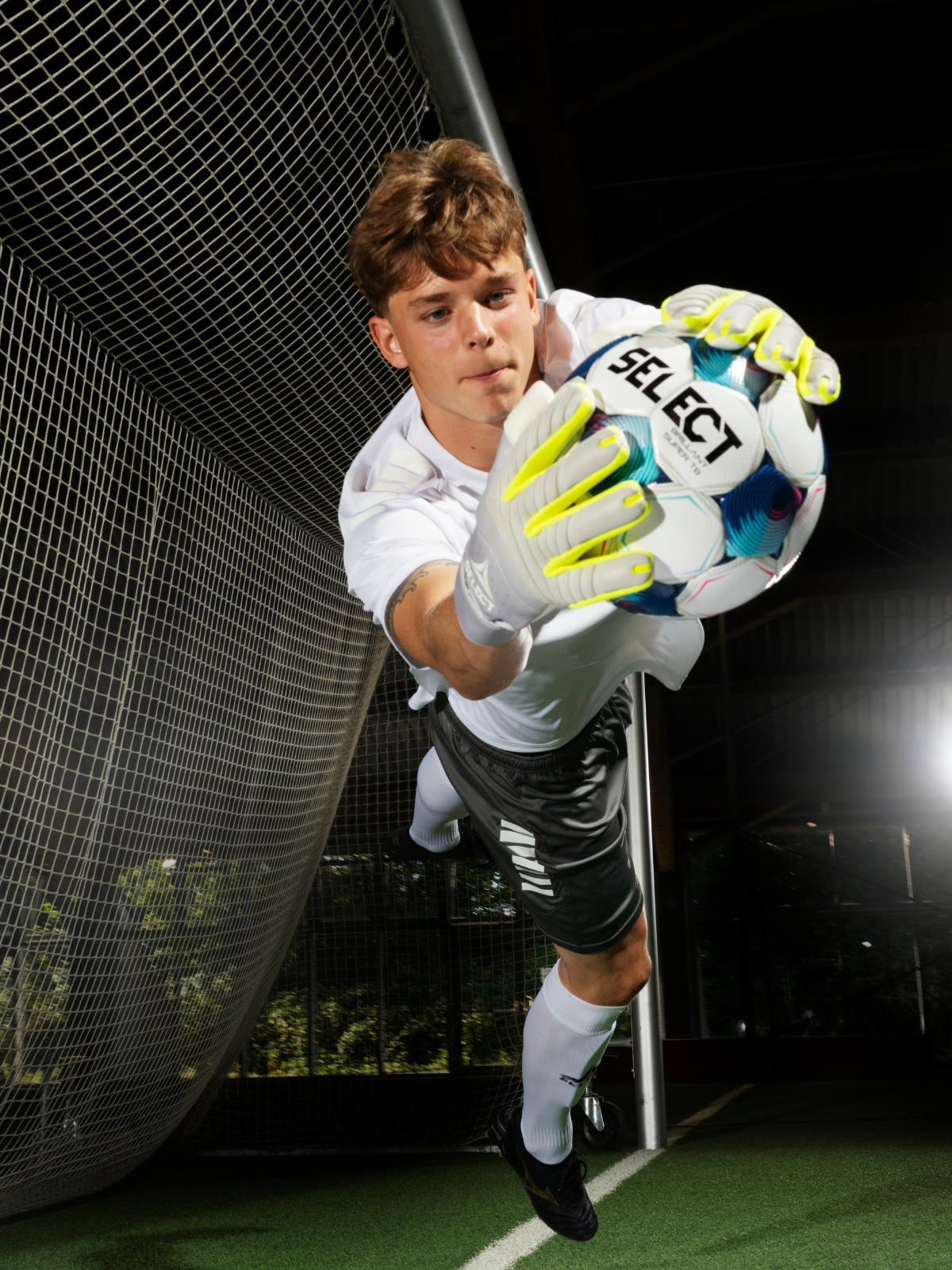 Goalkeeper catching a Select soccer ball in front of a net