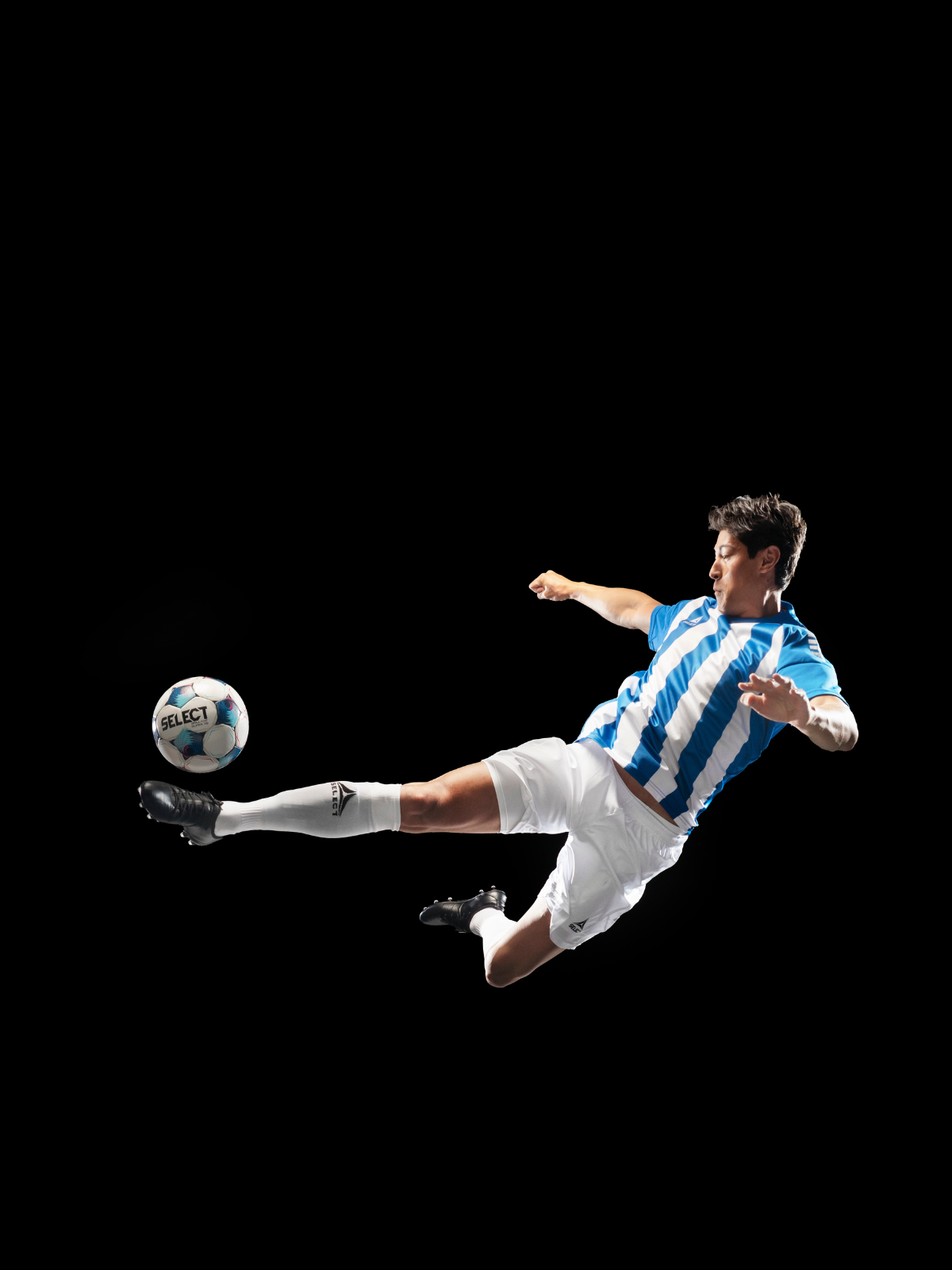 Soccer player wearing blue and white striped jersey and white shorts and sock kicking a soccer ball in the air on a black background. Select branded