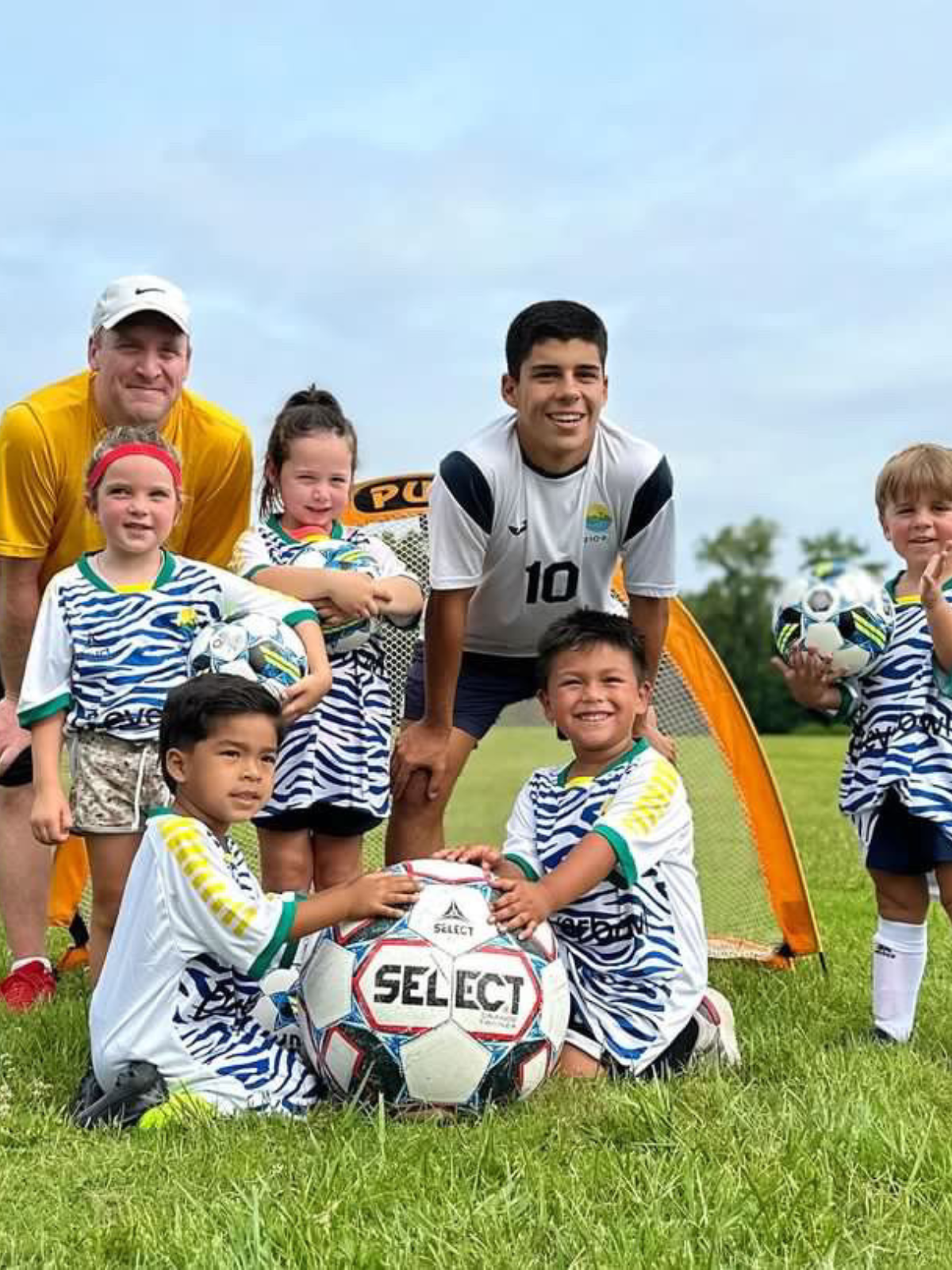 Youth soccer team on a field posing for a photo with a large 'Select' soccer ball