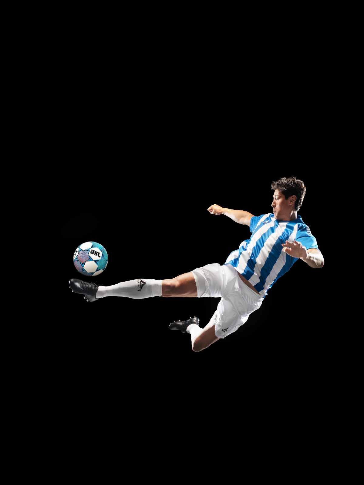 Soccer player in mid-air kicking a soccer ball on a black background